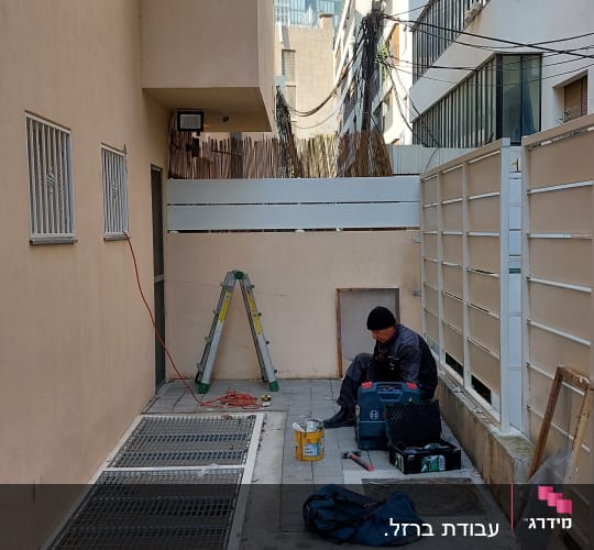 אדם יושב ליד סולם וכלי עבודה בחצר בניין